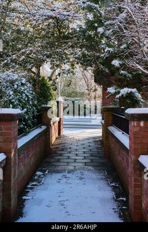 Percorso innevato sotto arco alberato delimitato da muri in mattoni di Cheshire con ringhiere in ferro Foto Stock