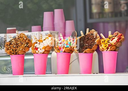 diverse varietà di gelato in coni di cialda con marmesh, noci, dolci, cocco e gocce di cioccolato in tazze rosa Foto Stock