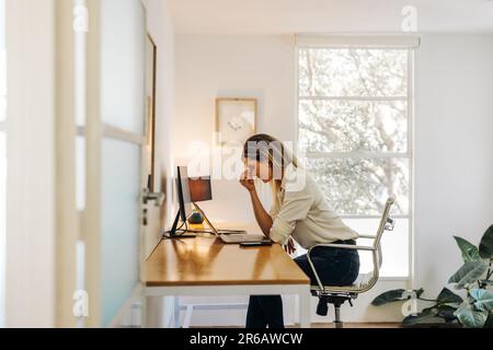Donna d'affari esausta che ha un mal di testa nel suo ufficio. Donna d'affari sovraccarica, che si trova davanti a un notebook e si trova in una situazione di fatica. Foto Stock