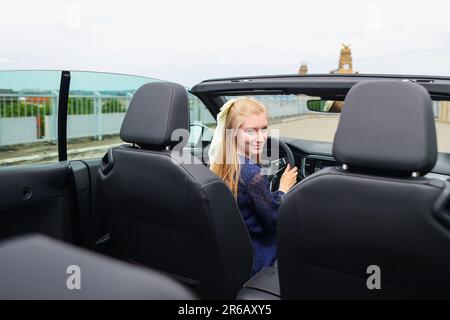 Giovane donna seduta in cabrio e guida in riserva. Foto Stock