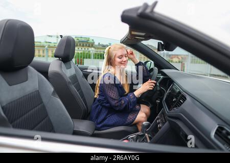 Giovane donna seduta in cabrio e guida in riserva. Foto Stock