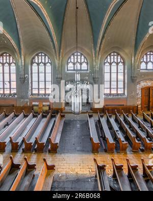 Una foto di un vecchio interno della chiesa con tradizionali zampe di legno disposte in modo ordinato e illuminate da belle vetrate Foto Stock