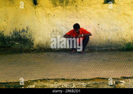 India, Aurangabad - 28 marzo 2018: L'uomo si siede sui suoi hapunches e sceglie intentemente il lavoro guardando il telefono. Foto Stock