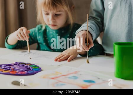 Due sorelle carine, i compagni di classe stanno dipingendo sul tavolo. Bambina bambini con spazzola a scuola. Buon adorabile preschooler, 4 e 7 anni bambino in soggiorno. Concetto di scuola domestica, facendo i compiti a casa Foto Stock