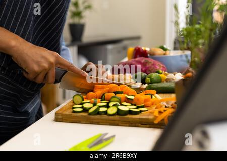 Sezione centrale della donna biraciale preparare il cibo in cucina tritare verdure Foto Stock