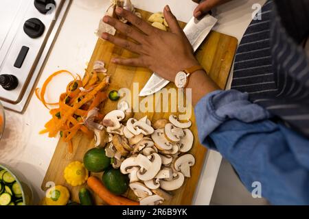 Parte centrale della donna biraciale in grembiule preparare il cibo in cucina schiacciare gli spicchi d'aglio Foto Stock