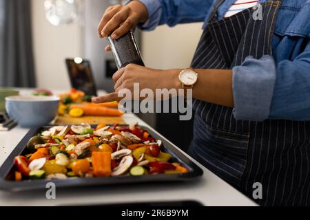 Sezione centrale della donna biraciale in grembiule preparazione del cibo in cucina condimenti vegetali Foto Stock