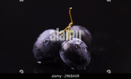 Primo piano di tre bacche di uva scura con gocce d'acqua. Foto Stock