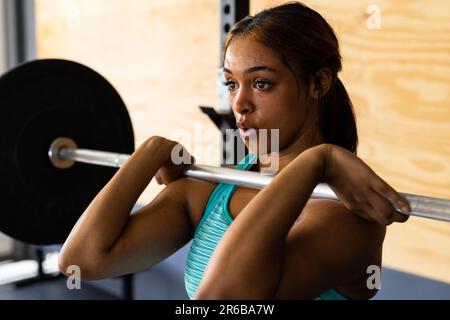 Primo piano di una giovane donna biraciale dedicata sollevamento barbell fiducioso nel centro benessere, copia spazio Foto Stock