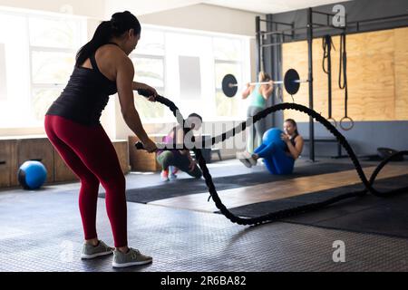 Vista laterale di una giovane donna caucasica dedicata all'esercizio con corde da battaglia nel centro benessere, spazio copia Foto Stock