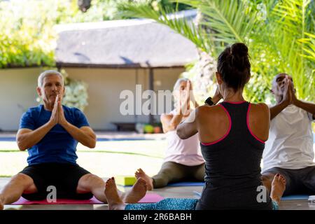 Ha messo a fuoco diversi anziani che esercitano in classe pilates con l'allenatore femminile Foto Stock