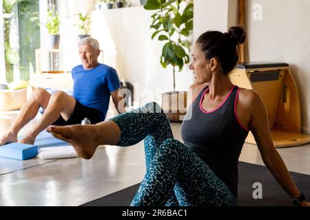 Uomo anziano caucasico focalizzato che si esercita in classe pilates con allenatore femminile Foto Stock