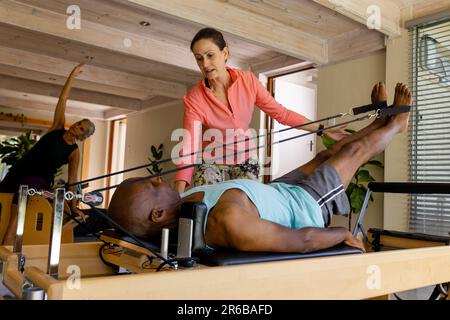 Ha messo a fuoco diversi anziani utilizzando l'attrezzatura da ginnastica in classe pilates con allenatore femminile Foto Stock