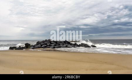 Una serena spiaggia caratterizzata da una collezione di rocce arrotondate e levigate sparse nelle acque poco profonde della costa Foto Stock