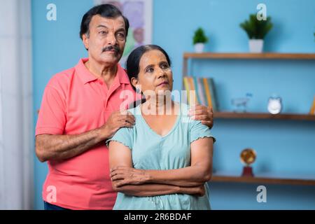 Indiano premuroso coppia anziana guardando lontano dalla macchina fotografica da stare in piedi a casa - concetto di problemi familiari, debito finanziario e legame Foto Stock