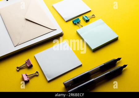 Disposizione piatta di penne nere, buste e carta bianca con spazio per la copia su sfondo giallo. Materiali scolastici, scrittura, colorazione, disegno, apprendimento, scuola Foto Stock