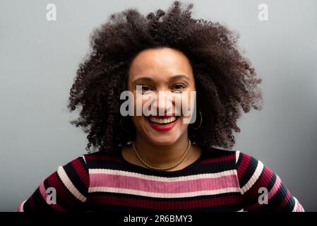 Ritratto facciale di bella giovane donna con capelli ricci. Isolato su sfondo grigio chiaro. Foto Stock