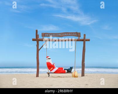 Un Babbo Natale jolly godendosi una giornata alla spiaggia mentre si siede in un altalena. Foto Stock