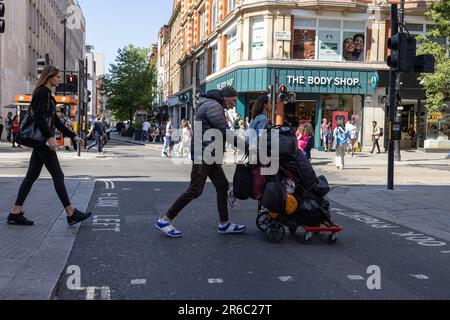 Un senzatetto spinge un carrello contenente le sue cose lungo Oxford Street, nel West End di Londra, Inghilterra, Regno Unito Foto Stock