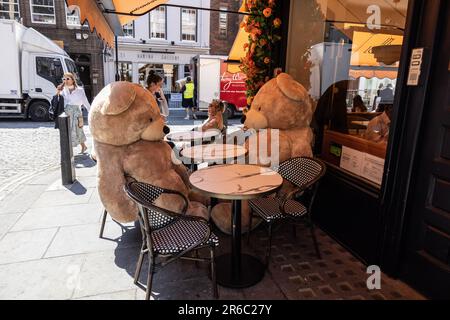 Due grandi orsi giocattolo seduti ai tavoli fuori da un caffè, nel West End di Londra in una calda giornata estiva durante una mini-ondata di caldo nel giugno 2023, Londra, Inghilterra, Regno Unito Foto Stock