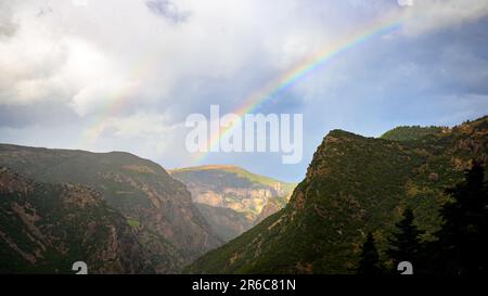 Uno spettacolare arcobaleno arcate su un lussureggiante paesaggio di montagna, incorniciato da una bancarella di alberi Foto Stock