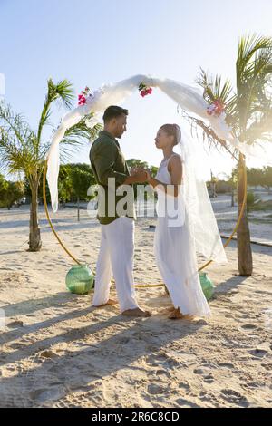 Vista laterale del giovane sposo caucasico che indossa l'anello di nozze per sposarsi durante la cerimonia nuziale in spiaggia Foto Stock
