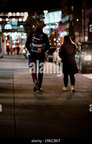 Due figure adulte che camminano lungo un marciapiede illuminato di notte in città Foto Stock