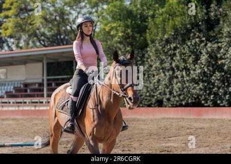 Primo piano di una giovane donna che cavalca un cavallo in un centro equestre Foto Stock