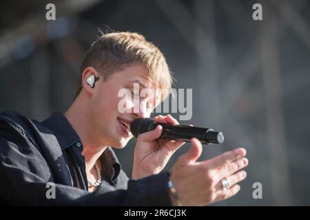 Un giovane uomo che indossa auricolari e cuffie che canta in un microfono e si esibisce appassionatamente in un ambiente di studio Foto Stock