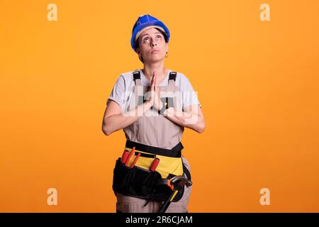 Donna ingegnere di costruzione che fa preghiera mani simbolo sulla macchina fotografica, chiedendo e chiedendo nuovi progetti di ristrutturazione. Donna lavoratore di costruzione sperando di lavorare sul cantiere e progetto di ristrutturazione. Foto Stock