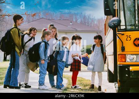 Una linea di studenti delle scuole medie e elementari che si preparano a salire a bordo di un bus scolastico Foto Stock