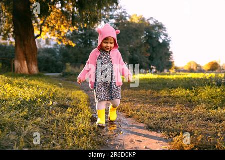 Bambina che indossa stivali di gomma camminando in pozza all'aperto Foto Stock