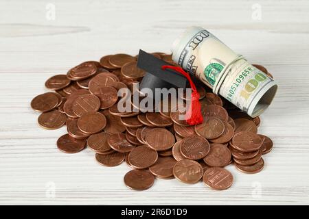 Concetto di borsa di studio. Tappo graduato, monete e banconote in dollari su tavolo di legno bianco Foto Stock