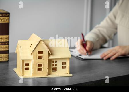 Concetti di costruzione e di diritto fondiario. Donna che scrive in appunti a tabella grigia, fuoco sul modello della casa. Spazio per il testo Foto Stock