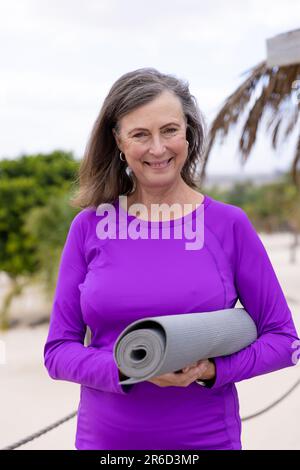 Ritratto di donna anziana caucasica sorridente con materassino per esercizi in piedi presso la località turistica Foto Stock