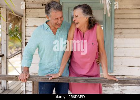 Allegra coppia caucasica che ride e sta in piedi in ringhiera nel balcone esterno del cottage Foto Stock