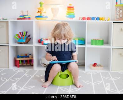 Bambina seduta su un vasino con il tablet. Addestramento del vasino. Formazione sulla toilette Foto Stock