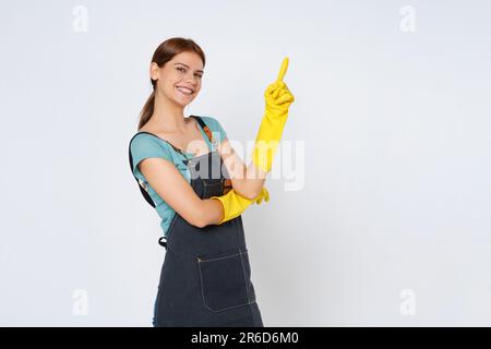 Giovane donna che indossa guanti di gomma gialla per la protezione delle mani e punta a uno spazio vuoto isolato su sfondo bianco. Foto Stock