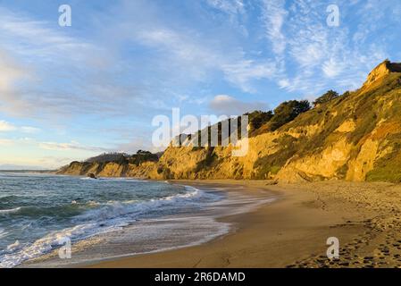 Spiaggia di mare con scogliere sotto il cielo blu e nuvole bianche. Foto Stock