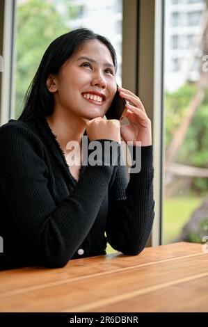 Un ritratto di una giovane donna asiatica felice che chiama qualcuno, ama parlare al telefono mentre si rilassa nel bar. Foto Stock