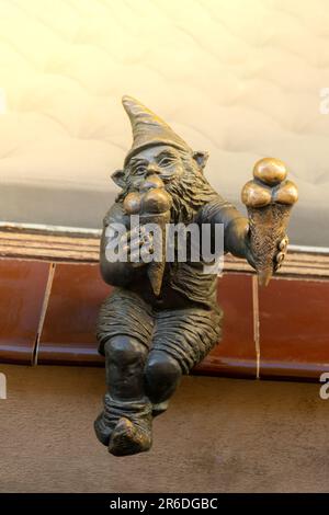 Nana mangia gelato sul davanzale di una vecchia pasticceria. Piccole figure in bronzo di gnomi sulle strade di Breslavia. Europa Figura in bronzo miniatura di uno gnome. Simbolo di Breslavia. Attrazione turistica Foto Stock