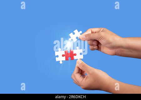 Mani che tengono jigsaw puzzle pezzo con sfondo blu chiaro, business di successo, strategia di soluzione, concetto di partnership lavoro di squadra Foto Stock