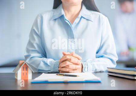 il venditore domestico della donna discute i particolari del progetto dell'alloggiamento al cliente nell'ufficio di vendite di progetto sul tavolo là è una miniatura grigia hou Foto Stock