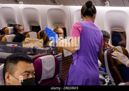 L'equipaggio di cabina della Thai Airways indossa un facemask che serve i passeggeri nella sezione Economy sul volo internazionale da Manila a Bangkok Foto Stock