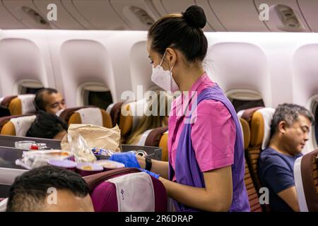 L'equipaggio di cabina della Thai Airways indossa un facemask che serve i passeggeri nella sezione Economy sul volo internazionale da Manila a Bangkok Foto Stock