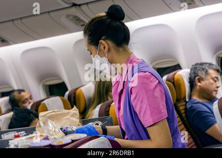 L'equipaggio di cabina della Thai Airways indossa un facemask che serve i passeggeri nella sezione Economy sul volo internazionale da Manila a Bangkok Foto Stock