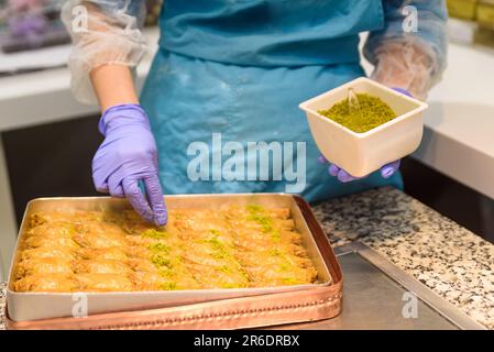Primo piano delle mani preparare dolci tradizionali turchi di baklava con pistacchio all'interno di una panetteria a Istanbul. Fabbricazione di baklava Foto Stock