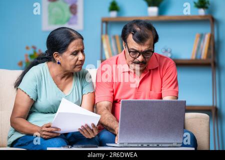 Coppia di anziani indiani che discute controllando i documenti o le fatture usando il laptop nel paese - concetto della tecnologia, della pianificazione finanziaria e della relazione Foto Stock