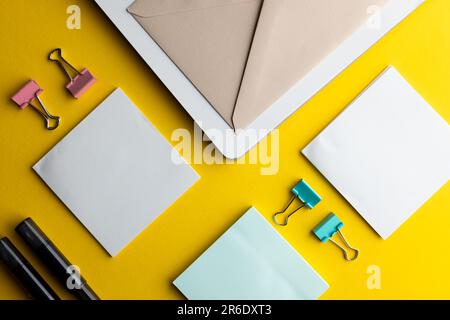 Disposizione piatta di penne nere, buste e carta bianca con spazio per la copia su sfondo giallo. Materiali scolastici, scrittura, colorazione, disegno, apprendimento, scuola Foto Stock