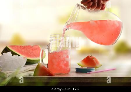 Persona che serve bevanda rinfrescante di anguria preparata di fresco con ghiaccio tritato da una caraffa su una panca della cucina. Vista frontale. Composizione orizzontale. Foto Stock